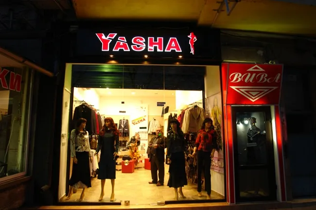 Светеща табела „Yasha“ над вход на магазин, нощем